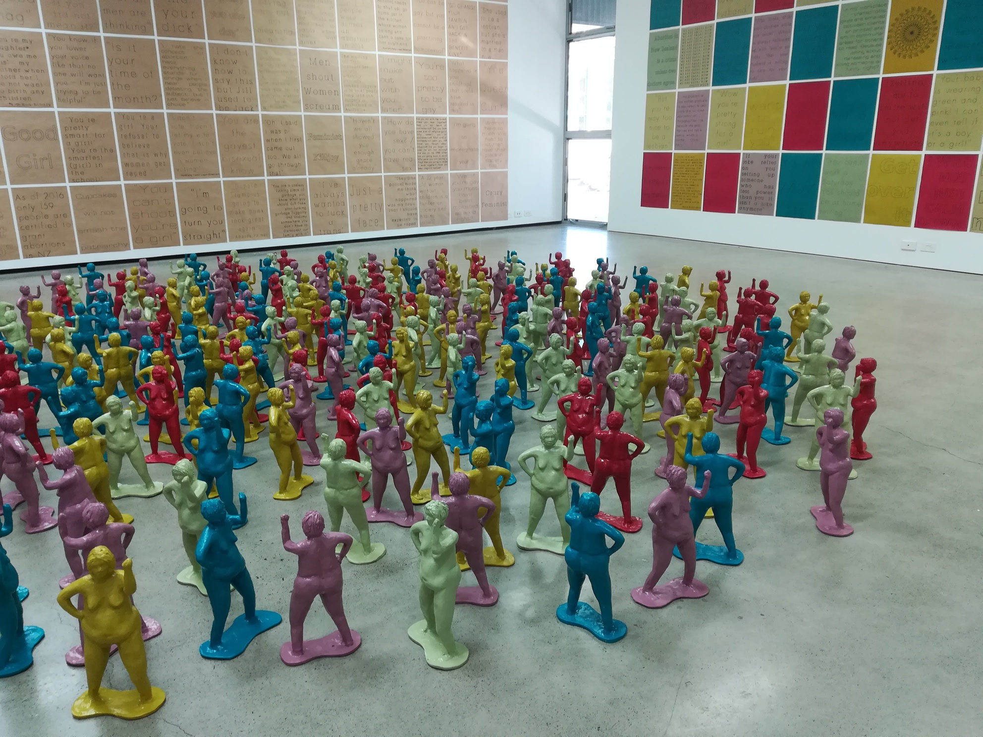 Installation photo of multi-coloured ceramic berthas, with two walls of posters